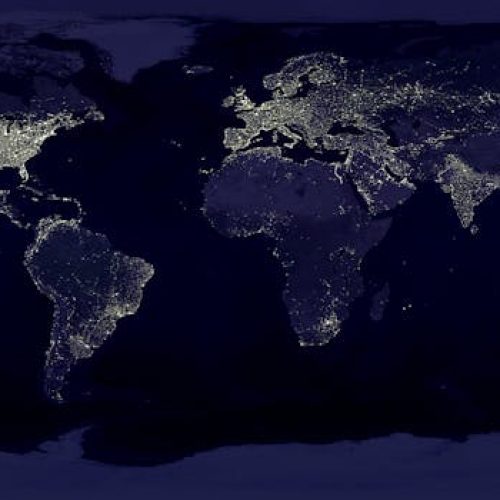 Satellite view of Earth at night with illuminated cities across continents.