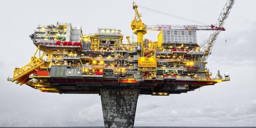 A well-lit offshore oil platform against a cloudy sky in Norway's waters.