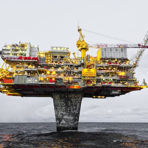 A well-lit offshore oil platform against a cloudy sky in Norway's waters.