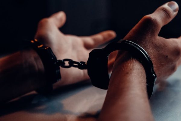 A close-up of human hands handcuffed on a table with a dark background, depicting law enforcement themes.