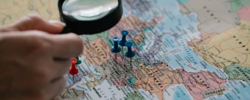 Magnifying glass focuses on pins highlighting travel destinations on a world map.